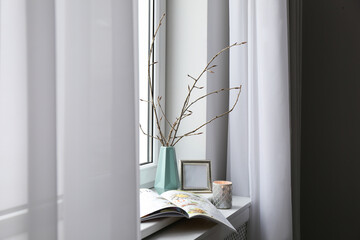 Tree twigs in ceramic vase, decor and magazine on window sill at home