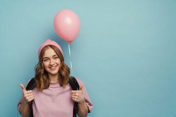 Wall Mural - Young white student girl showing thumb up while posing with balloon