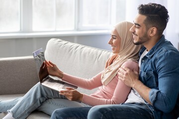 Wall Mural - Side view of muslim couple using laptop at home