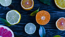 Dark Background With Slices Of Tangerines Lemons Oranges Limes Citrus Fruits And Green Leaves Close Up On A Wooden Background Top View	