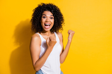 Sticker - Photo of lucky charming young dark skin woman dressed white tank-top rising fists isolated yellow color background