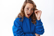 © Cookie Studio - Portrait of pretty girl in glasses looking surprised, saying wow with excited face, checking out awesome promo offer, standing in blue hoodie against white background