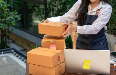 Young smiling beautiful owner asian woman freelance sme business online shopping working on laptop computer with parcel box on desk at home - SME business online and delivery concept