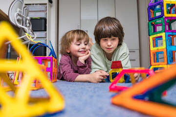 two brothers spend time together at home during quarantine. boys playing magnetic constructor toy. c
