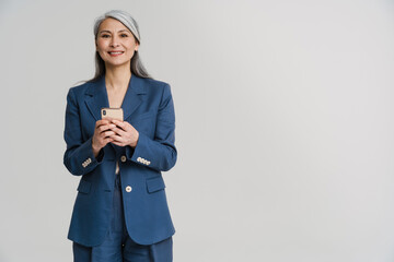 asian mature woman in jacket smiling while using mobile phone