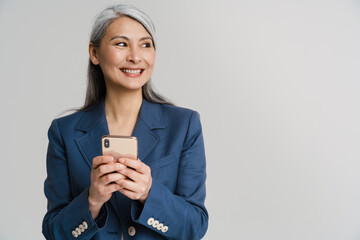 asian mature woman in jacket smiling while using mobile phone
