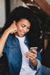 © InsideCreativeHouse - Smiling afro young woman surfing the Internet at home. Smiling african american woman using smartphone at home, messaging or browsing social networks while relaxing on couch