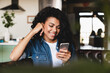© InsideCreativeHouse - Cheerful african teenage girl using smart phone sitting on the sofa.Smiling african american woman using smartphone at home, messaging or browsing social networks while relaxing on couch