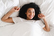 © InsideCreativeHouse - Young african girl waking up in her white bed in the morning. Cheerful young woman lying on bed playing with blanket and looking at camera. African girl feeling fresh after nap on bed with copy space.