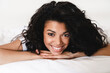© InsideCreativeHouse - Close up portrait of an afro young woman lying on the white bed. Lets start new day. Young African woman in tank top lying in bed.