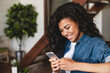 Beautiful african-american woman using smart phone in the living room. Beautiful afro american woman sitting at the desk in a home office and using a smart phone.