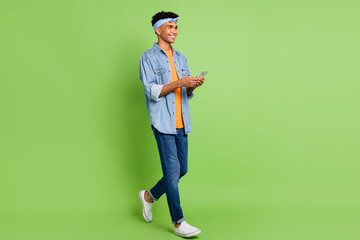 Sticker - Photo of guy hold smartphone look empty walk wear headband jeans shirt sneakers isolated green color background