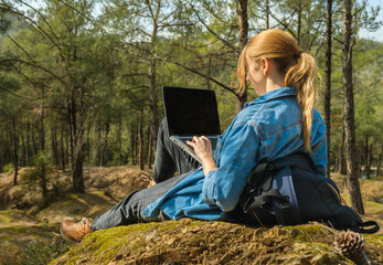 Young woman sitting on ground at forest and working on laptop .