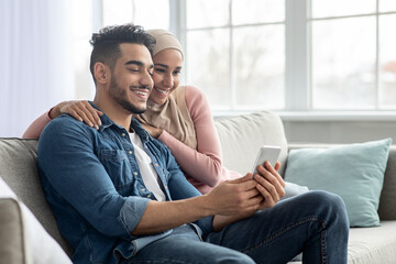 Happy middle-eastern couple using mobile phone at home