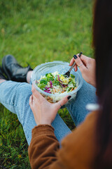 Wall Mural - Close-up of a salad bowl on teenager girl legs. She is sit on grass enjoying nature. Vertical shot.