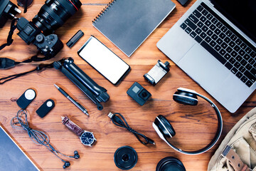 Top view bag with a digital camera, charger, mockup-phone, lens, video camera, USB, personal laptop, book, pen, remote control, and electronics camera accessory photography concept on wood background