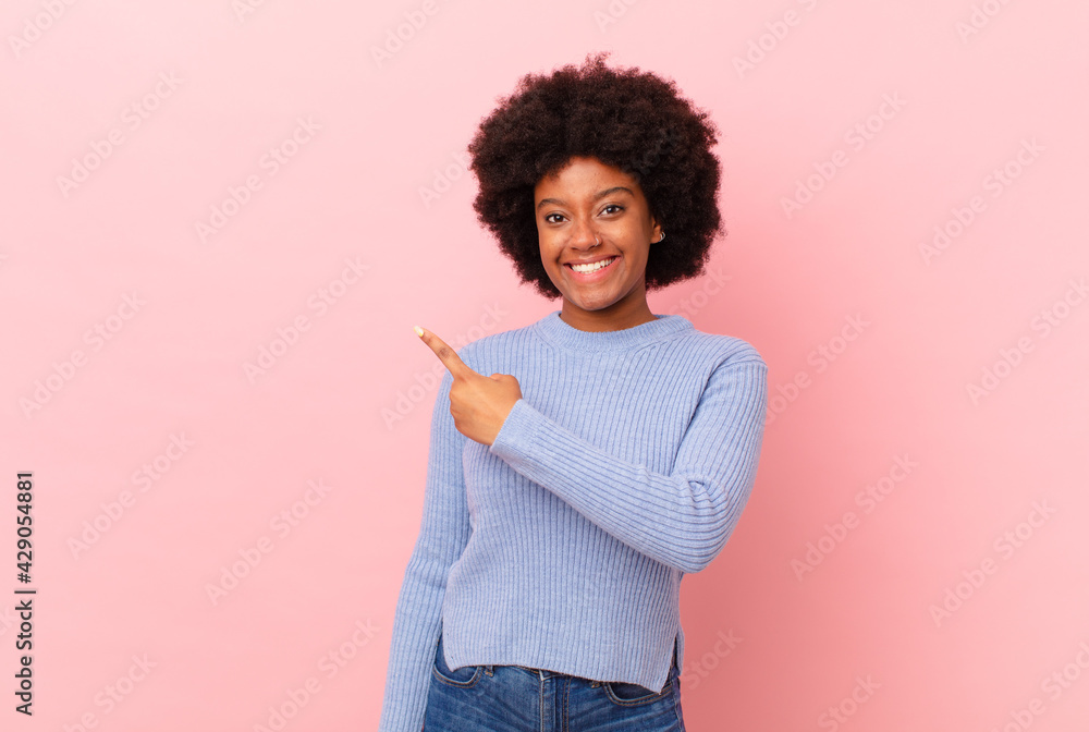 afro black woman smiling cheerfully, feeling happy and pointing to the side and upwards, showing object in copy space - obrazy, fototapety, plakaty 