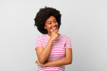 Wall Mural - afro black woman smiling with a happy, confident expression with hand on chin, wondering and looking to the side