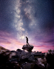 Wall Mural - a man standing on a rock as the milky way galaxy rises into the night sky at dusk. photo composite