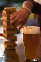 Poster - Vertical shot of a glass of beer and a hand playing with wooden blocks on the table