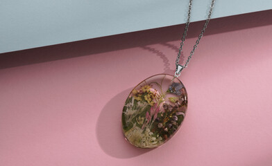 Epoxy Resin necklace pendant with natural flowers inside on pastel colors background