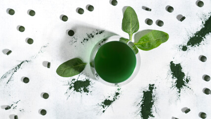 Healthy green spirulina drink in the glass with spirulina chlorella pills, algae powder and spinach leaves. Superfood, detox drink. Healthy care concept. Top view. Horizontal orientation.