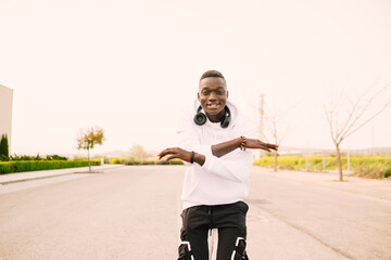 Wall Mural - Young african American black man with afro hair dancing in the middle of the street wearing a white sweatshirt, black pants and wireless headphones. Happy and joy attitude