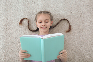 Sticker - Cute little girl reading book on floor at home, top view