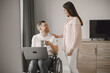 © prostooleh - Young man in wheelchair using laptop and girlfriend hugging him at home