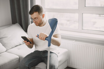 Young man with walking stick talk by phone indoors