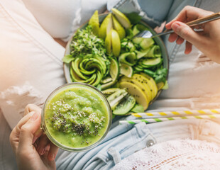 Wall Mural - Woman in jeans holding fresh healthy green salad with avocado, kiwi, apple, cucumber, pear, greens and sesame on light background. Healthy food, clean eating, Buddha bowl salad, top view, detox