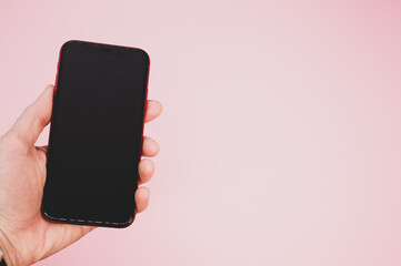 Wall Mural - Closeup shot of a hand holding a smartphone against a pink background