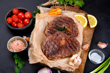 Wall Mural - Delicious prepared meat steaks with seasoning and herbs on dark background.