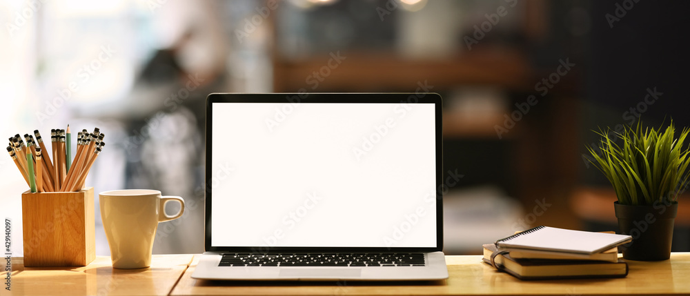 Front view computer laptop with empty screen, coffee cup, pencil holder, notebook and house plant on wooden table. - obrazy, fototapety, plakaty 
