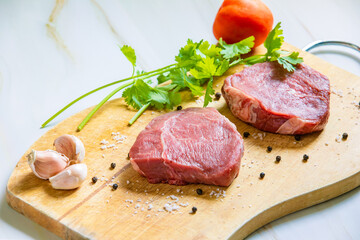 Raw beef filet Mignon steak or tenderloin on wooden board with pepper, salt, and vegetables