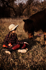 Little girl plays with horse in forest. Girl feeding apples to ponies outdoors. 