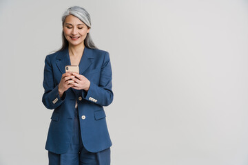 asian mature woman in jacket smiling while using mobile phone