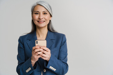 asian mature woman in jacket smiling while using mobile phone