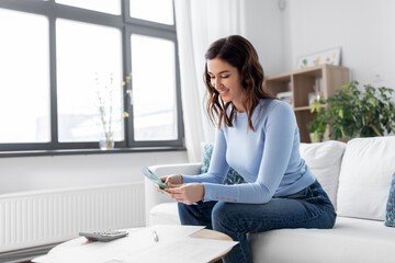 Wall Mural - business, finances, income and people concept - happy smiling woman with calculator and bills counting money at home