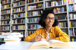 © Kateryna - Teenage african american female pretty student with glasses, studying while sits at the table in a college library, reads books to searching information for a lesson or exam, doing homework,looks away