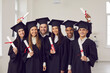 © Studio Romantic - Graduation from university concept. Group of happy multiracial students university graduates standing and looking at camera with dimplomas in hands over white wall in class at background