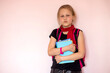 Portrait of a sad and sad schoolgirl with a backpack and stationery on a light background. Space for the text. Back to school. Preparing for school. Selective focus