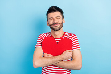 Sticker - Photo of cute dreamy young man dressed striped t-shirt embracing red paper heart closed eyes isolated blue color background