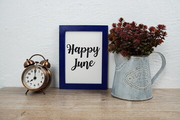 Wall Mural - happy june typography text with alarm clock and artificial plant decoration on wooden table and whit
