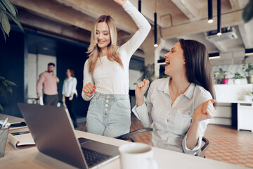 Wall Mural - Two young happy businesswomen celebrating project success in office