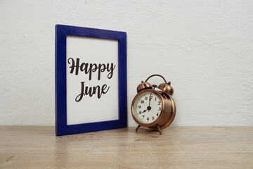 Wall Mural - happy june typography text and alarm clock on wooden table and white wall background