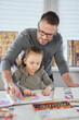 © boytsov - Attractive caring dad babysitter drawing with colored pencils crayons teaching girl sitting at the table, father enjoy helping child daughter doing homework at home during covid-19 quarantine