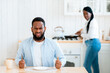 Starving Angry Black Man Waiting For Food At Table In Kitchen