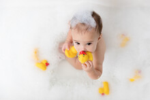 Cute Baby Girl In Bubble Bath Chewing On Rubber Ducks