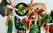 © Tijana - Table top view of woman hands making fresh salad in table full with organic vegetables. Directly above photo of housewife making lunch, mixing organic vegetables with mixing spoon at kitchen in home